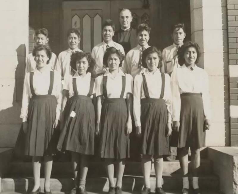 Une photo en noir et blanc d'un groupe d'élèves en uniforme et d'un homme debout devant un bâtiment.