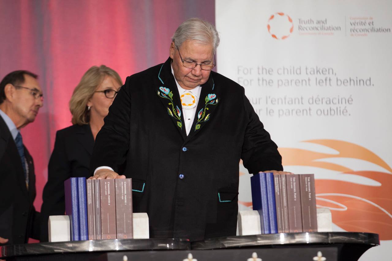 Justice Murray Sinclair bows his head as he rests his hands on copies of the Truth and Reconciliation Commission’s Final Report.