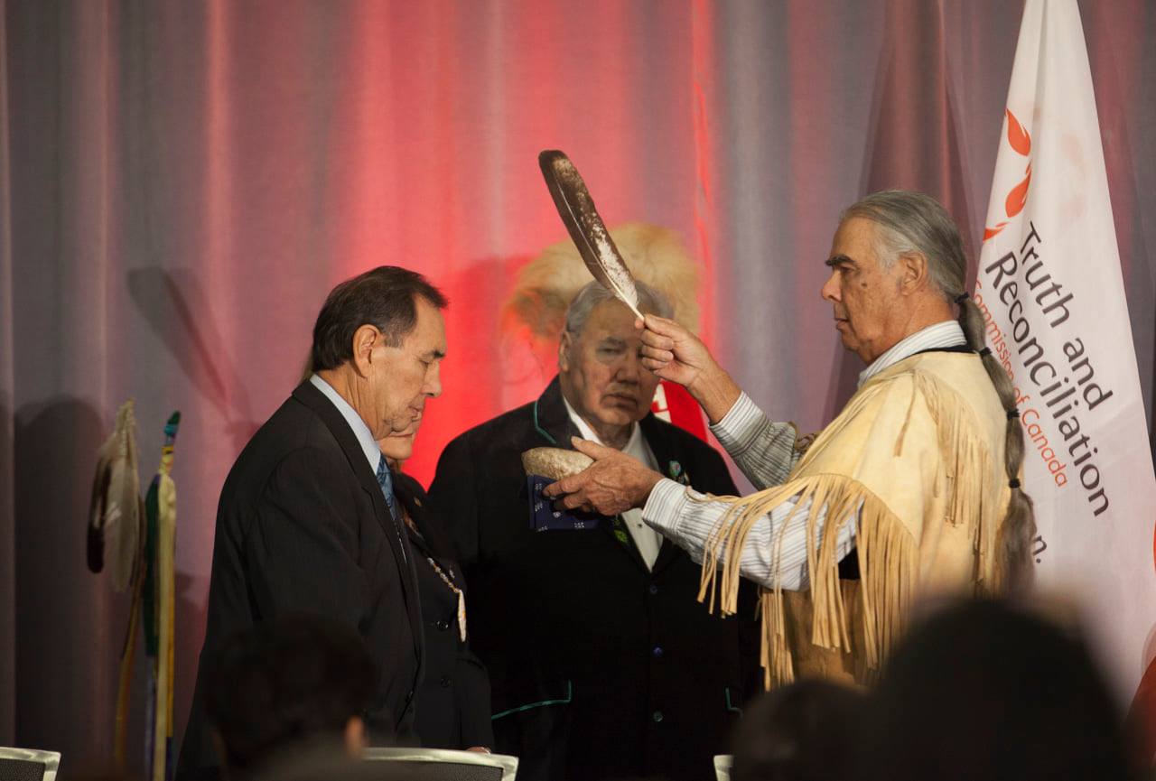 Elder smudges Chief Wilton Littlechild with Justice Murray Sinclair in the background.