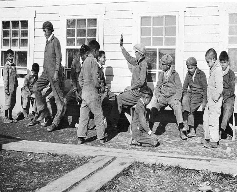 Group of students sitting and standing outside of Pelican Lake school building