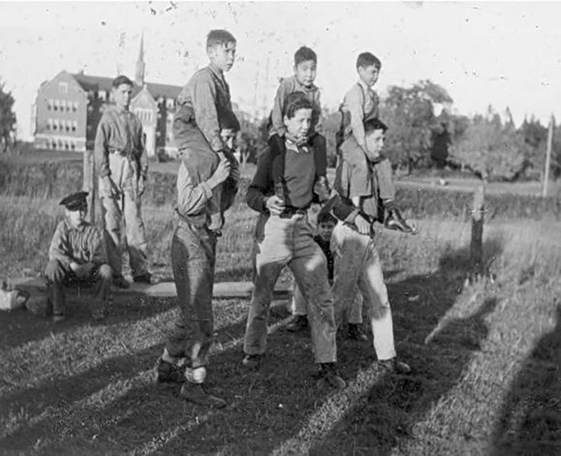 Group of students standing with other students on their shoulders outside Shingwauk school