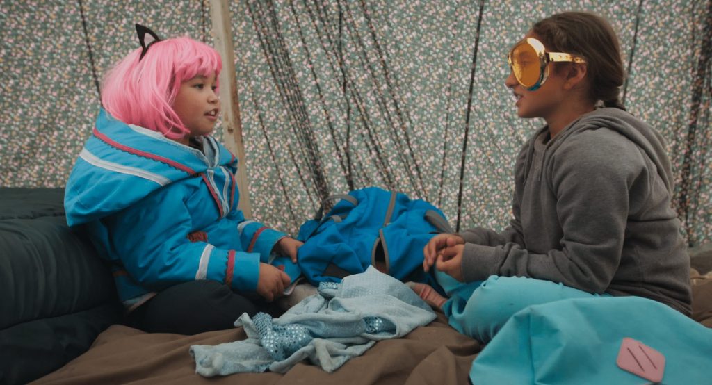 Photo de deux jeunes filles devant un fond en tissu à motifs assises sur des couvertures en train de discuter entre elles