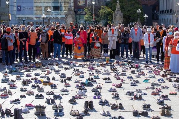 A crowd stands in front of shoes that honour missing and deceased Indigenous children.