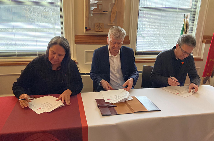 Representatives from the NCTR and the Oblates sit at a conference table, signing documents.