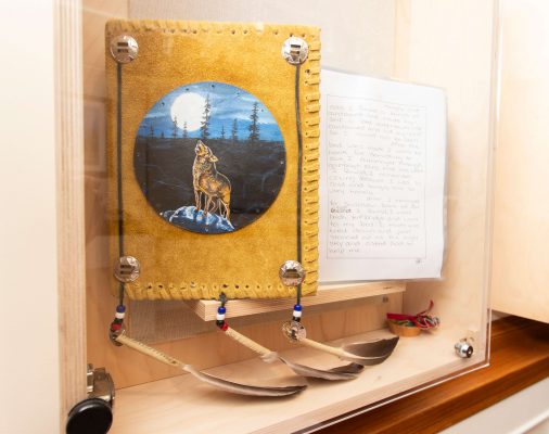 A leather-bound book adorned with eagle feathers and a circular painting of a wolf howling at the moon in the centre. The diary contains the handwritten residential school remembrances of Survivor Stanley Normand.