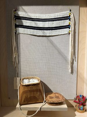 A wampum belt, alongside a woven basket depicting stylized animals and containing a declaration from the Sioux Lookout Coalition on Healing and Reconciliation.